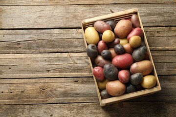 Different types of potatoes in crate on wooden table, top view. Space for text