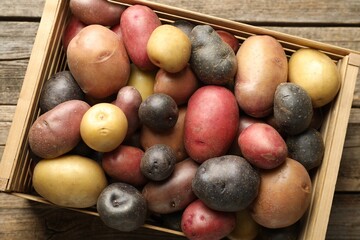 Different types of potatoes in crate on wooden table, top view