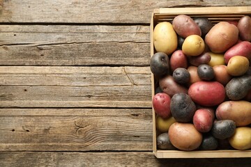 Different types of potatoes in crate on wooden table, top view. Space for text
