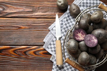 Raw purple potatoes in metal basket and knife on wooden table, flat lay. Space for text