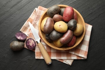 Different types of potatoes in bowl and knife on black table, flat lay