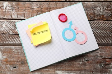 Sticky notes with phrase Sex Education, paper female and male gender symbols in notebook on wooden...