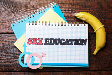 Notebooks with phrase Sex Education, paper female and male gender symbols, banana with condom on...