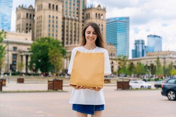 Smiling young woman holding blank eco paper shopping bag in city