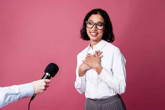 Confident young woman in a formal outfit being interviewed while expressing gratitude against a pink background