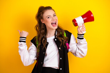 Cute cheerful student holding a megaphone against vibrant yellow background, expressing excitement...