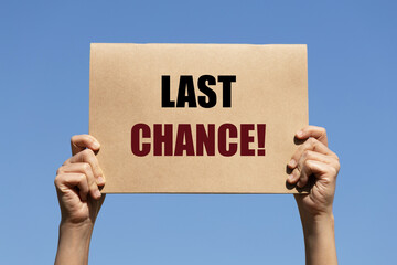 Last chance text on paper holding by a woman's hand with blue sky background