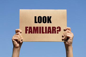 Look Familiar question text on paper holding by a woman's hand with blue sky background