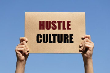 Hustle culture text on paper holding by a woman's hand with blue sky background