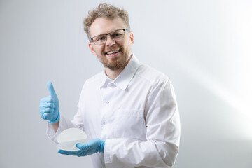 Male doctor holding silicone breast implants with thumbs up gesture, test quality