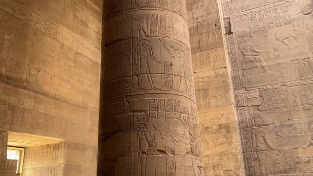 Intricately carved pillar at the Temple of Philae in Aswan, Egypt, depicting ancient Egyptian gods and goddesses in detailed reliefs.
