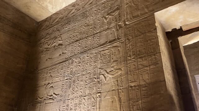 Wall at the Temple of Philae in Aswan, Egypt, with detailed reliefs depicting ancient Egyptian gods and goddesses in stone carvings.