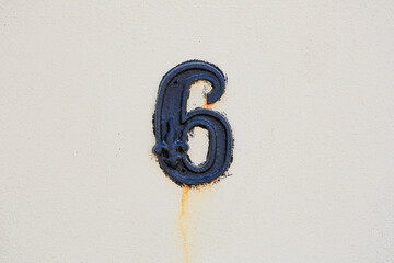 Decorative number 6 fixed on a light textured wall, showing weather stains and rustic detail. A...