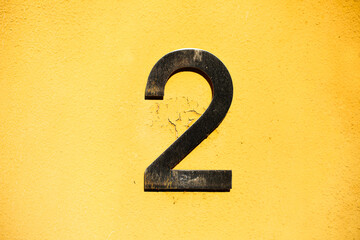 Bold number 2 mounted on a textured yellow wall, showing signs of weathering and age. A simple yet...