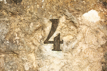 Rustic metallic number 4 affixed to a rough, weathered stone wall. The numeral has a patina finish...
