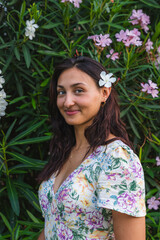 Portrait of a beautiful young woman with a flower in her hair, posing near a flowering oleander...