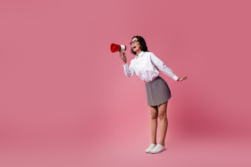 Young woman holding a megaphone in a stylish pose against a vibrant pink background, showcasing...