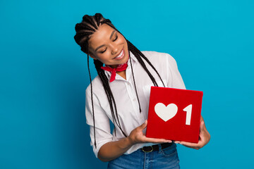 Young woman with braided hair holding a red heart sign on a blue background, expressing social...