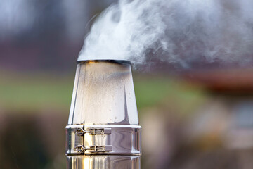 Steam rises from a metallic chimney in a rural setting during chilly early morning hours