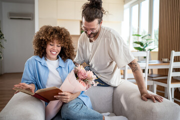 Happy couple sharing a book and flowers at home