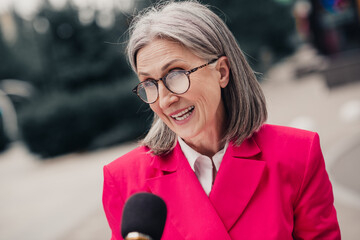 Confident and stylish mature woman in bright pink jacket smiling during outdoor urban interview on...