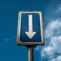 Weathered one way street sign pointing downwards against blue sky