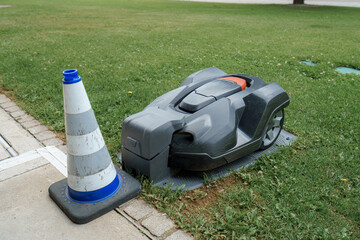 Robotic lawn mower parked near a traffic cone on a well-maintained lawn at a residential area