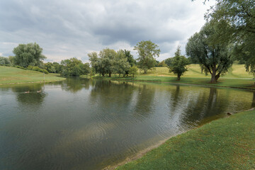 Serene lakeside view at a park during overcast afternoon with green trees and gentle water ripples
