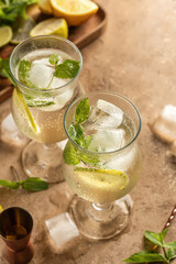 Mojito long rum drink with fresh mint, lemon juice, ice cubes and soda on brown textured background. Summer party cocktails with text space