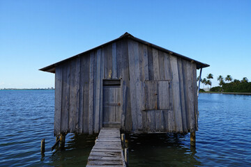 Seaside Wooden Shack Serene Coastal Structure on Stilts over Water with Clear Blue Sky and Tropical...