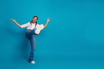 Youthful woman joyfully posing with one leg raised against a vibrant blue backdrop, showcasing...