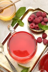 Tasty raspberry tea, berries, honey and mint on light grey table, flat lay
