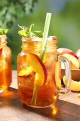 Refreshing iced peach tea with mint in mason jars on wooden table against blurred green background, closeup