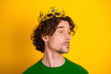 Portrait of a young man in a green sweater with a gold crown against a vibrant yellow background