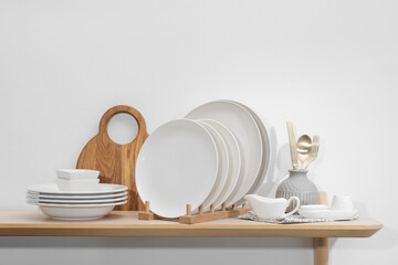 Clean dishware and cutting board on wooden table near white wall