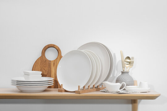 Clean dishware and cutting board on wooden table near white wall - Powered by Adobe