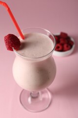 Tasty raspberry milkshake in glass and berries on pink background, closeup