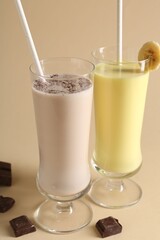 Different tasty milkshakes in glasses and pieces of chocolate on beige background, closeup