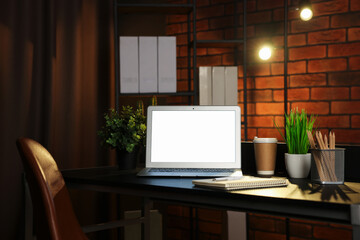 Laptop, takeaway paper cup, houseplants and stationery on black table near brick wall