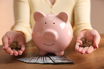 Woman with piggybank and money at wooden table, closeup