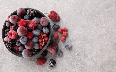 Mix of ripe frozen berries and bowl on grey textured table, flat lay. Space for text
