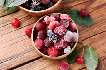 Mix of ripe frozen berries and green leaves on wooden table, flat lay