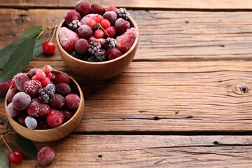 Mix of ripe frozen berries and green leaves on wooden table, closeup. Space for text