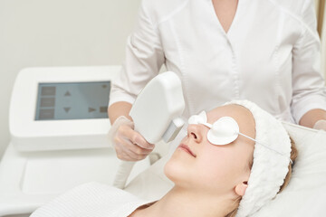 Young caucasian female receiving facial laser treatment at spa clinic for skin rejuvenation.