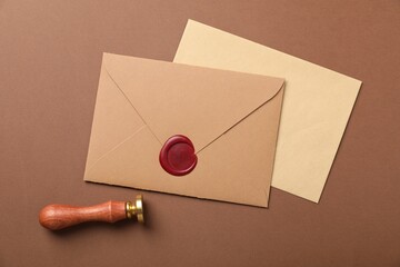 Envelopes with wax seal and stamp on brown background, flat lay