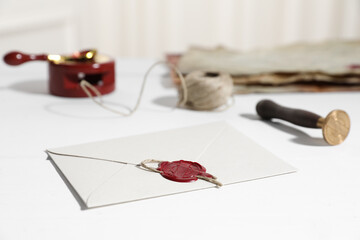 Envelope with wax seal and stamp on white wooden table, closeup