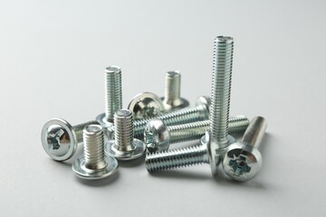 Many different metal bolts on light grey background, closeup. Hardware tool