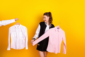 Young woman holding shirts on hangers against a vibrant yellow background, perfect for themes of...