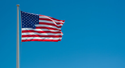 Fototapeta premium The American flag waves proudly against a vibrant, cloudless, bright blue sky.