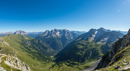 Fototapeta premium Panoramic alpine valley view, lush green valleys, and snow-capped mountain peaks under a clear blue sky.